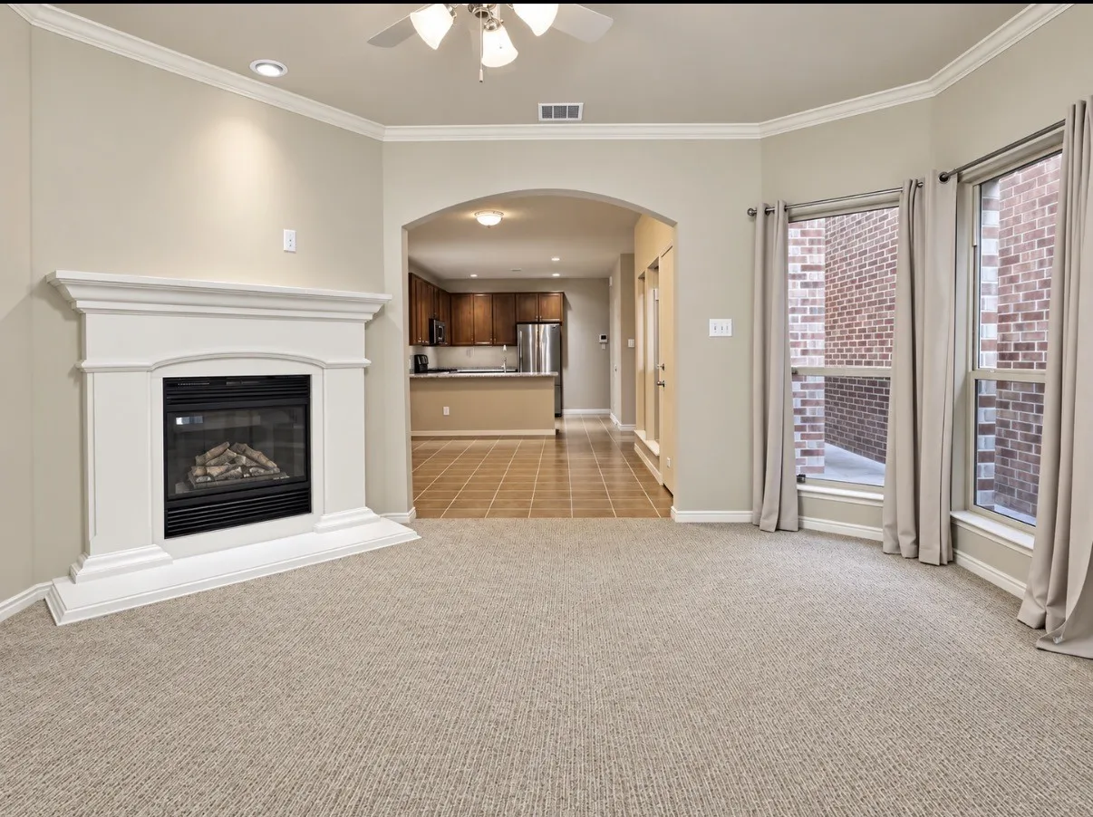 Living area featuring a white fireplace mantle with a central hearth, crown molding, arched entry, and large windows with natural light