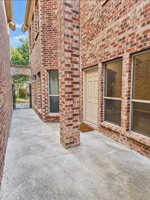 Full-brick exterior facade featuring a concrete patio, paneled entry door, vertical windows with brick sills, and a metal security gate
