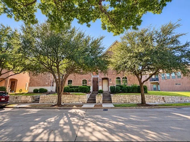 Brick exterior featuring arched windows, stone-faced retaining walls, dual staircases, and mature trees