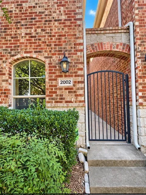 Brick exterior featuring a stone base, arched window with decorative muntins, wrought iron gate, and wall-mounted exterior sconce