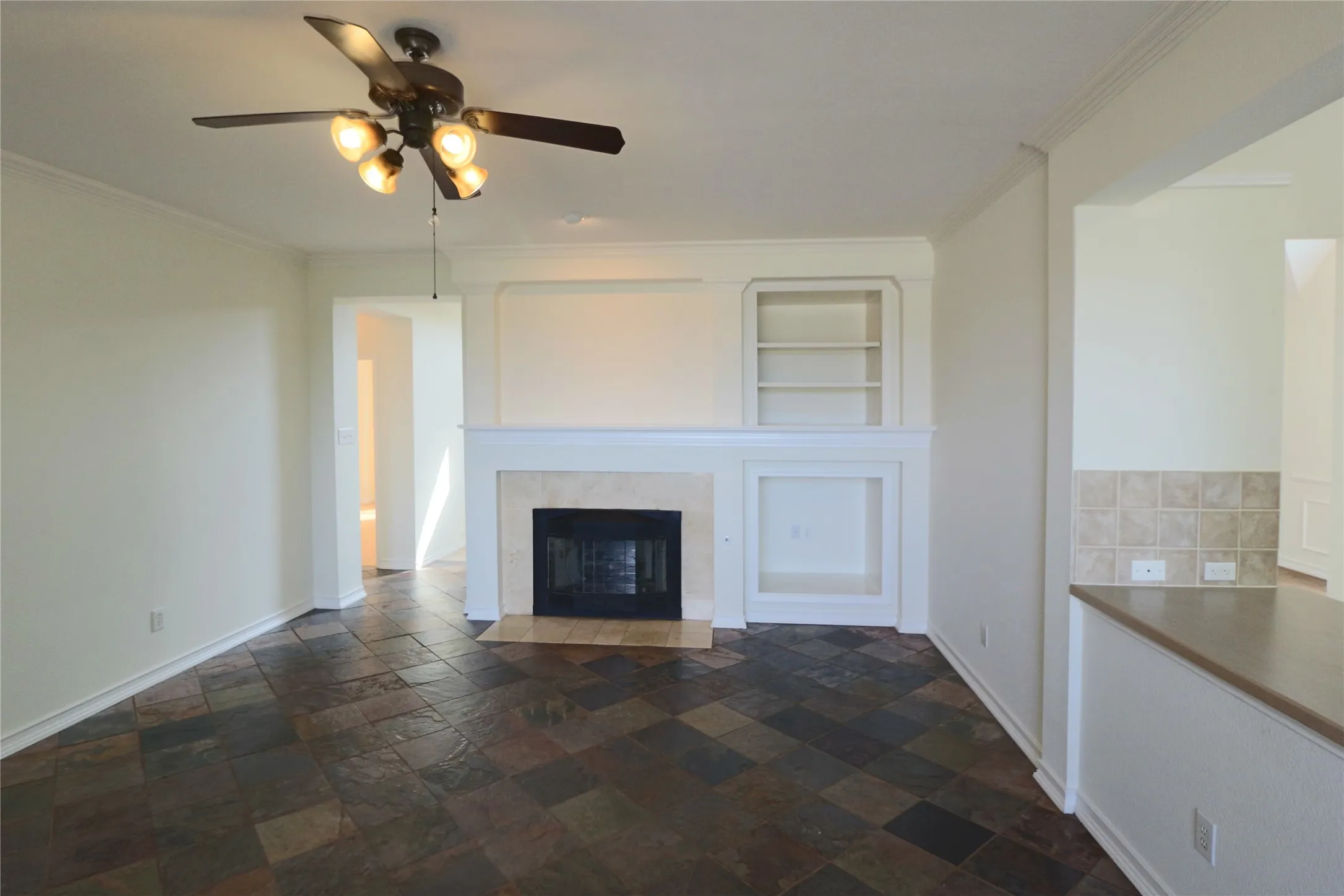 Living room with built in cabinets, fire place and ceiling fan, open to the kitchen.