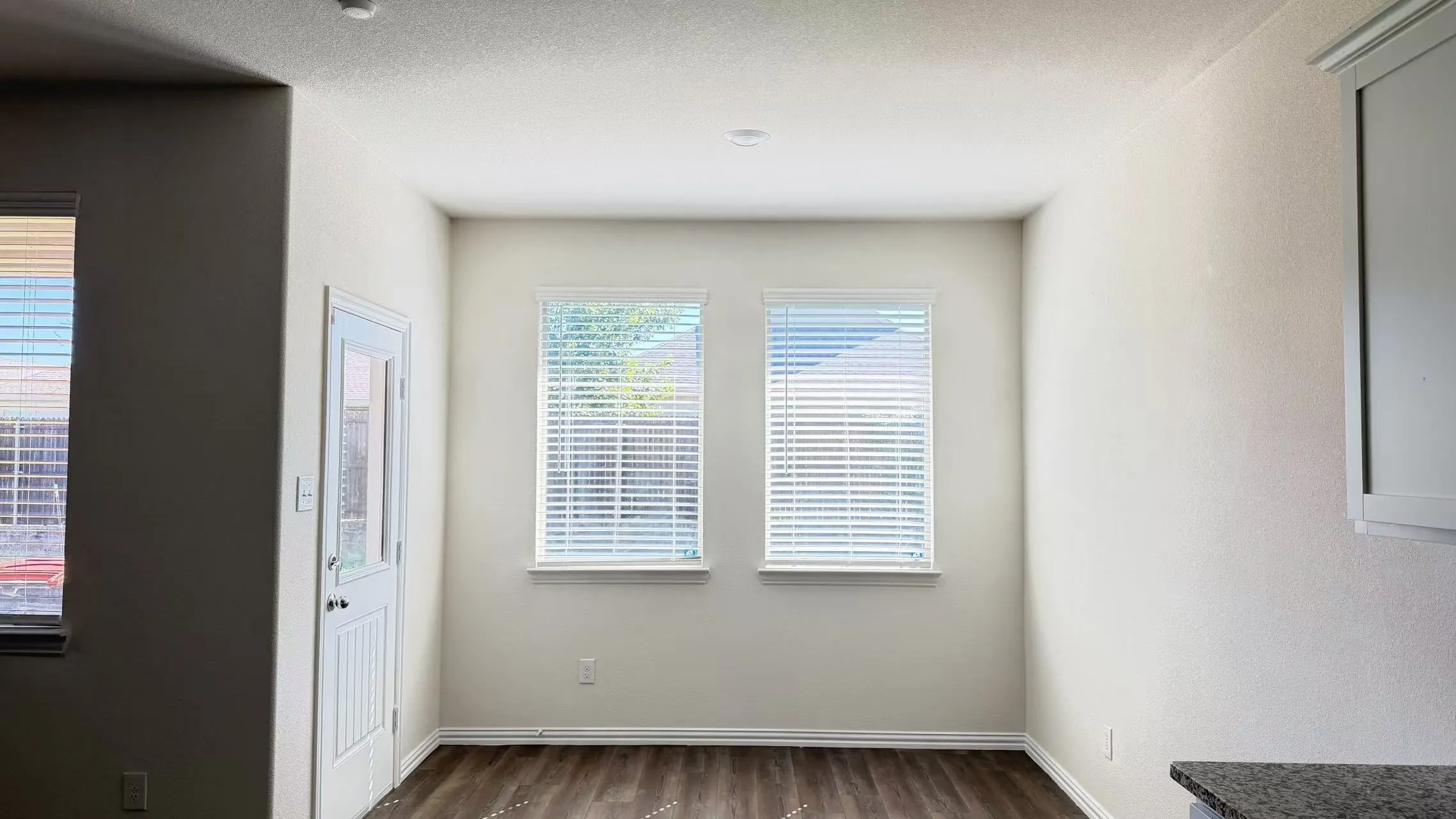 Neutral walls, wood-finish flooring, dual windows with blinds, and a glass-paneled exterior door