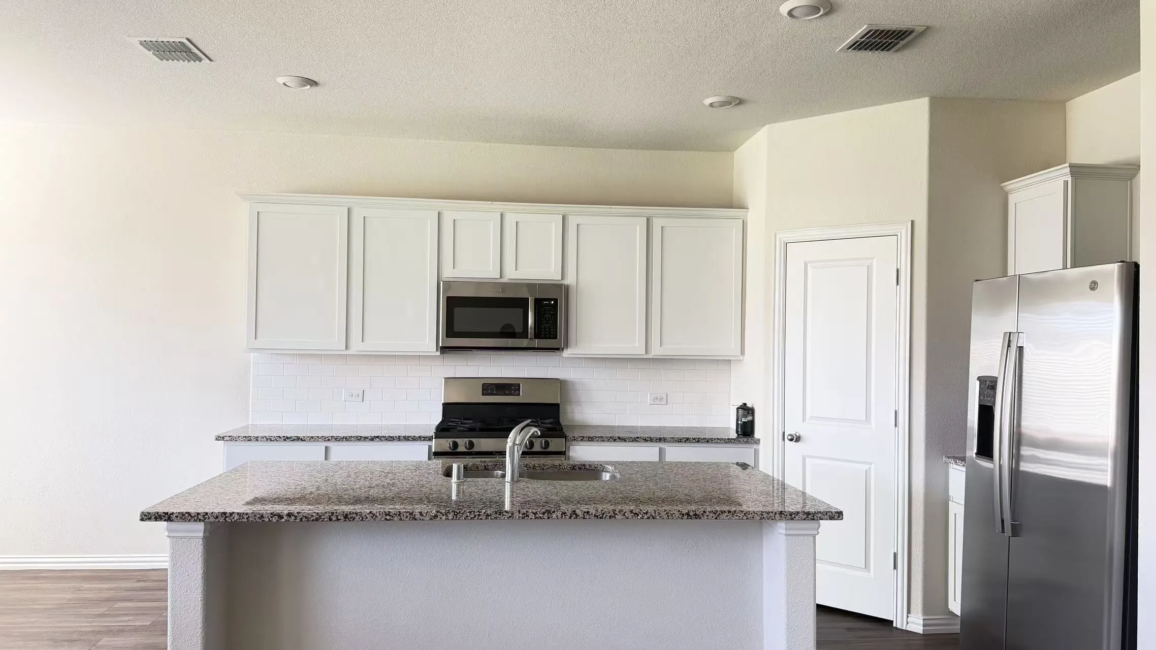 Kitchen featuring white shaker-style cabinetry, stone-finish countertops, stainless steel appliances, a center island with an integrated sink, and subway tile backsplash