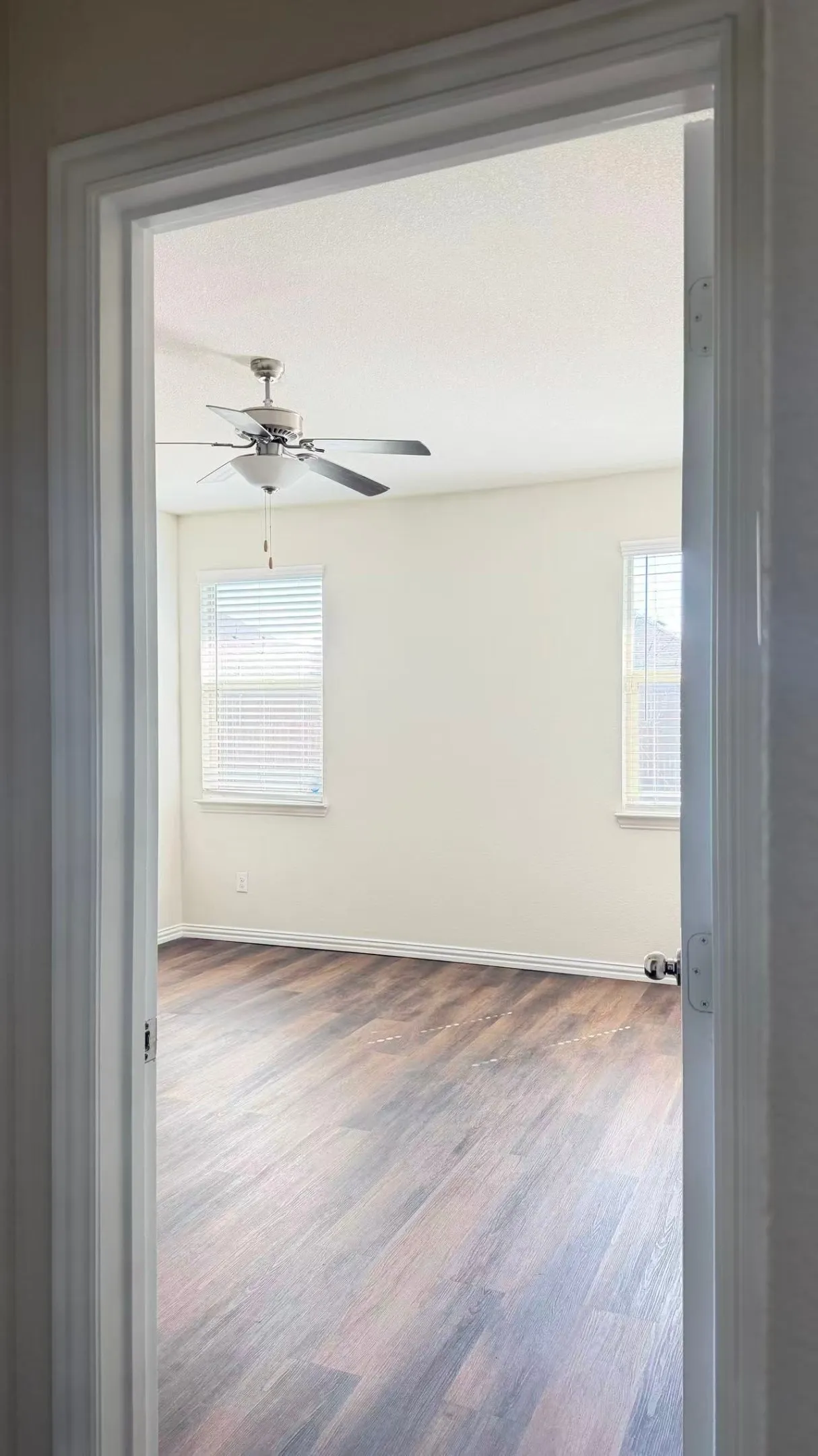 Room featuring wood-finish flooring, dual windows with horizontal blinds, and a multi-blade ceiling fan