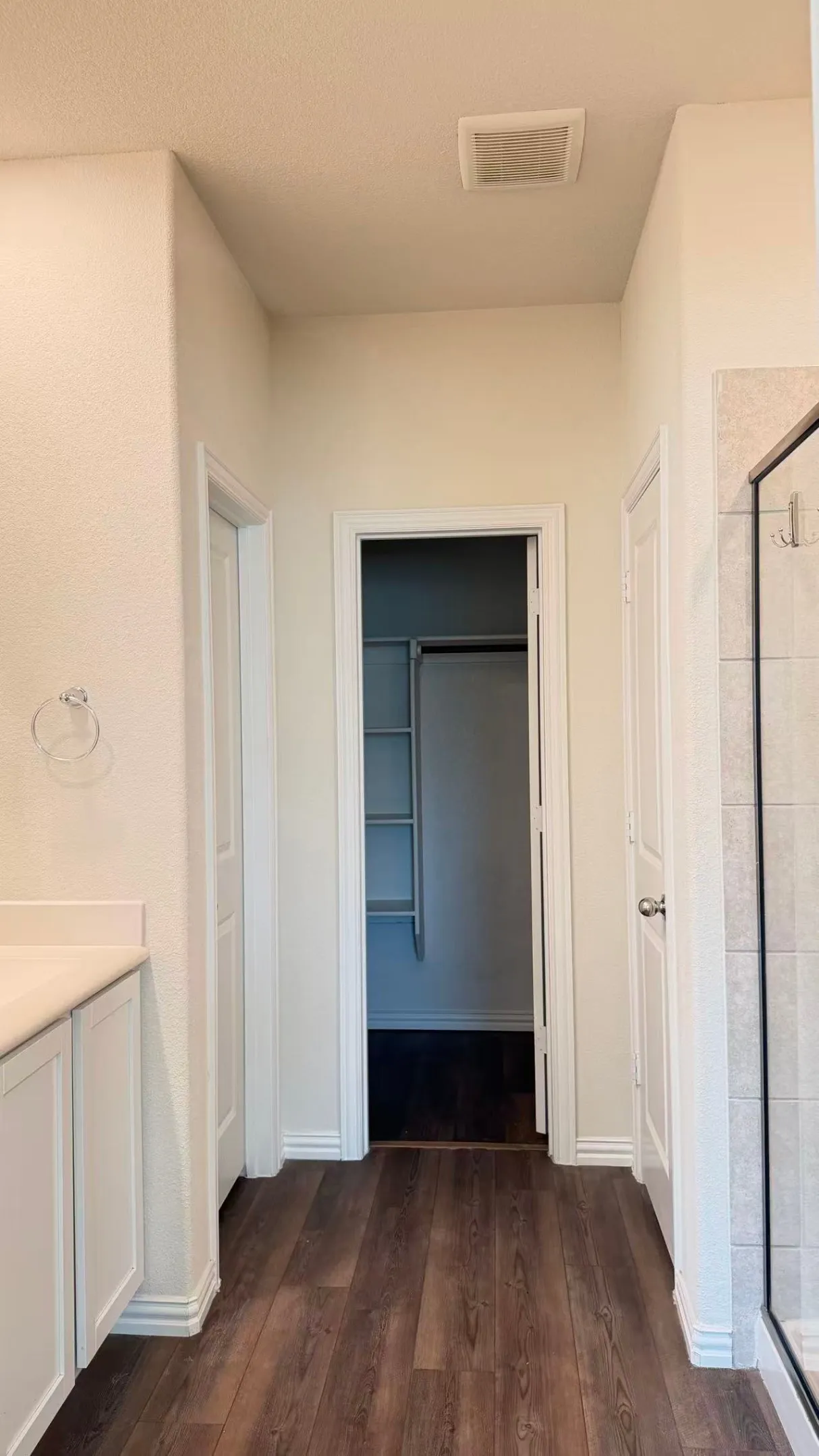 Wood-finish flooring, white built-in cabinetry, walk-in closet with integrated shelving, and tiled shower surround