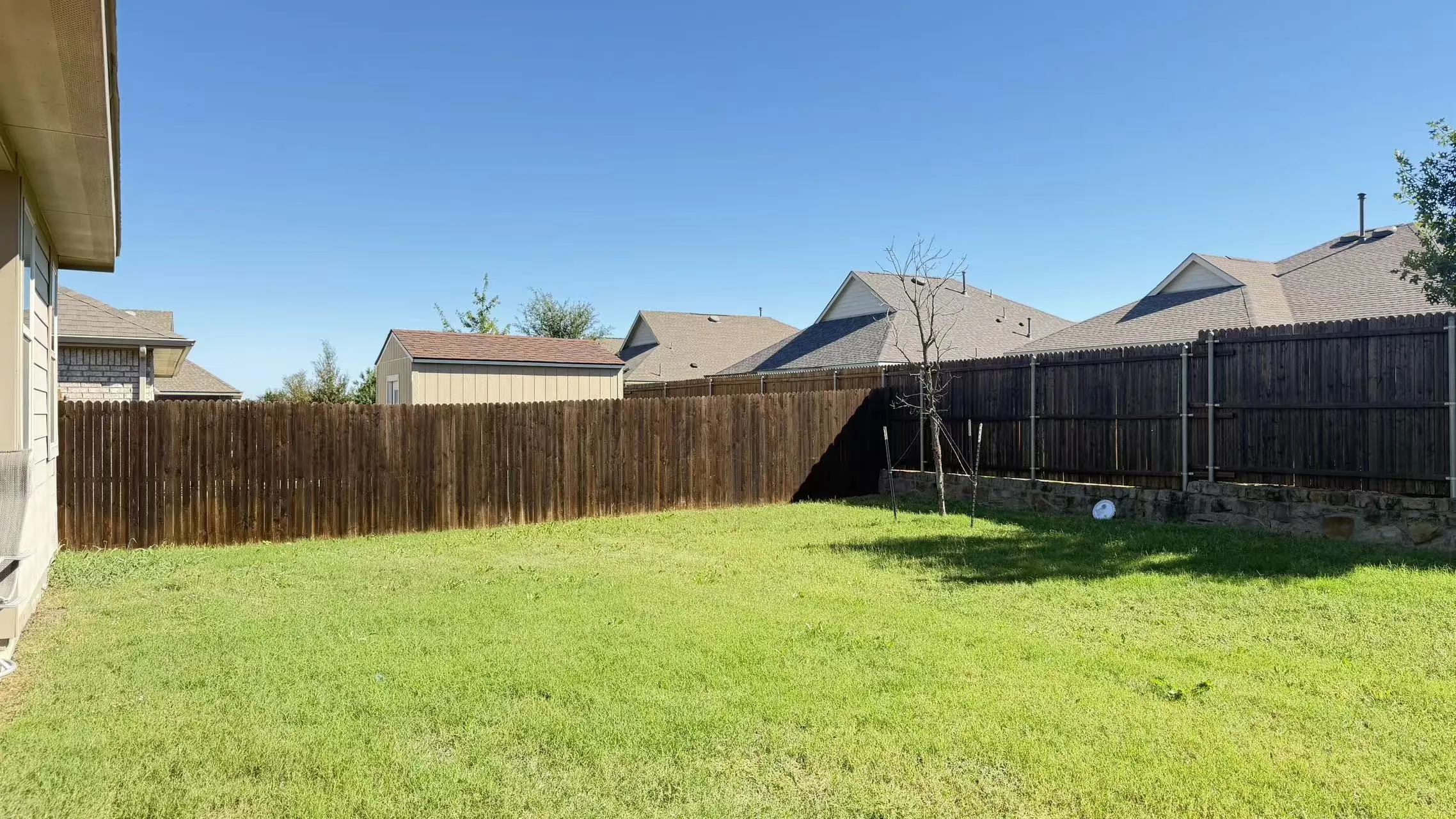 Backyard featuring a grass lawn, stained wood privacy fencing, and stone retaining wall