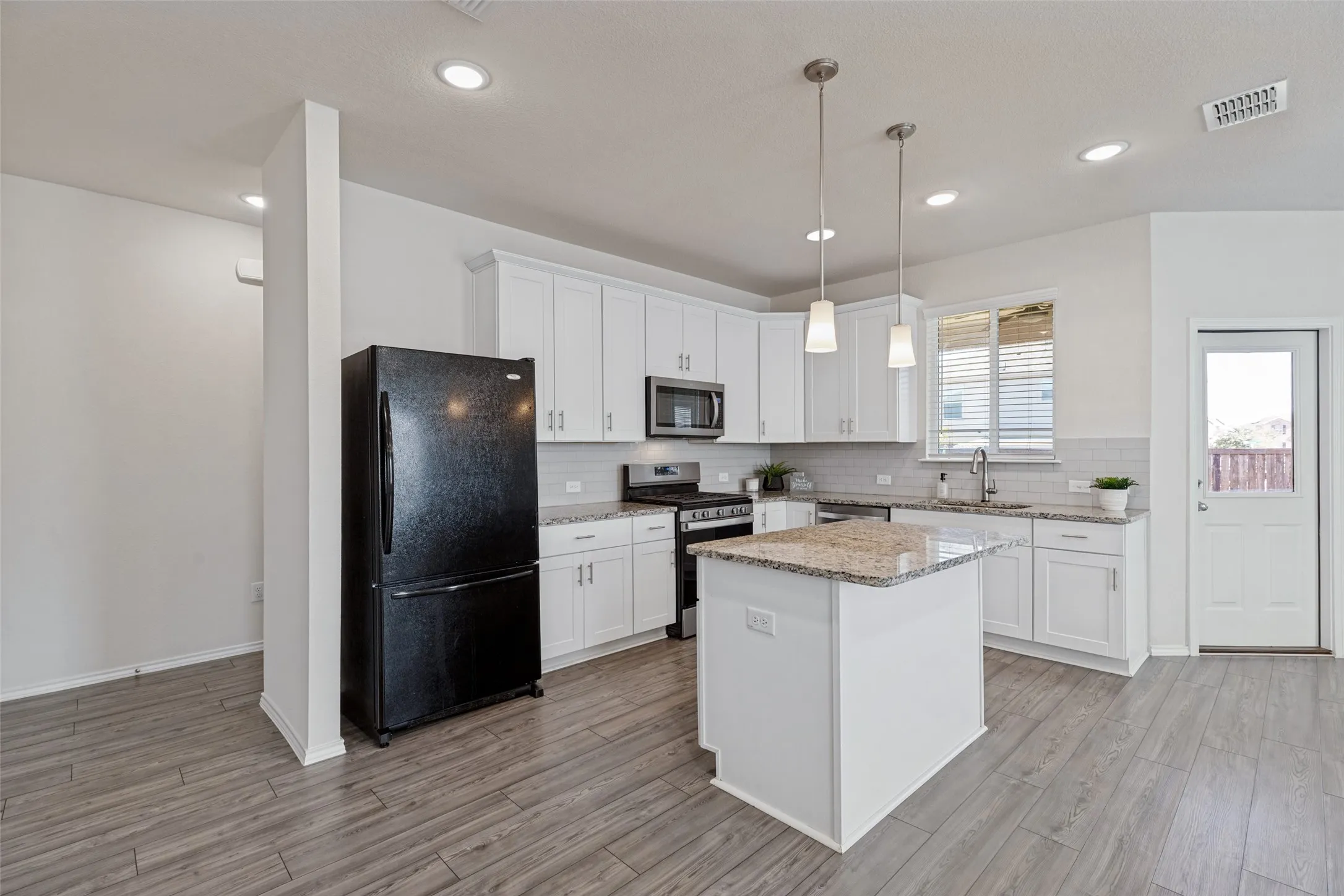Kitchen equipped with 42" cabinets, granite countertops, gas stove, decorative tile backsplash and pendant lights