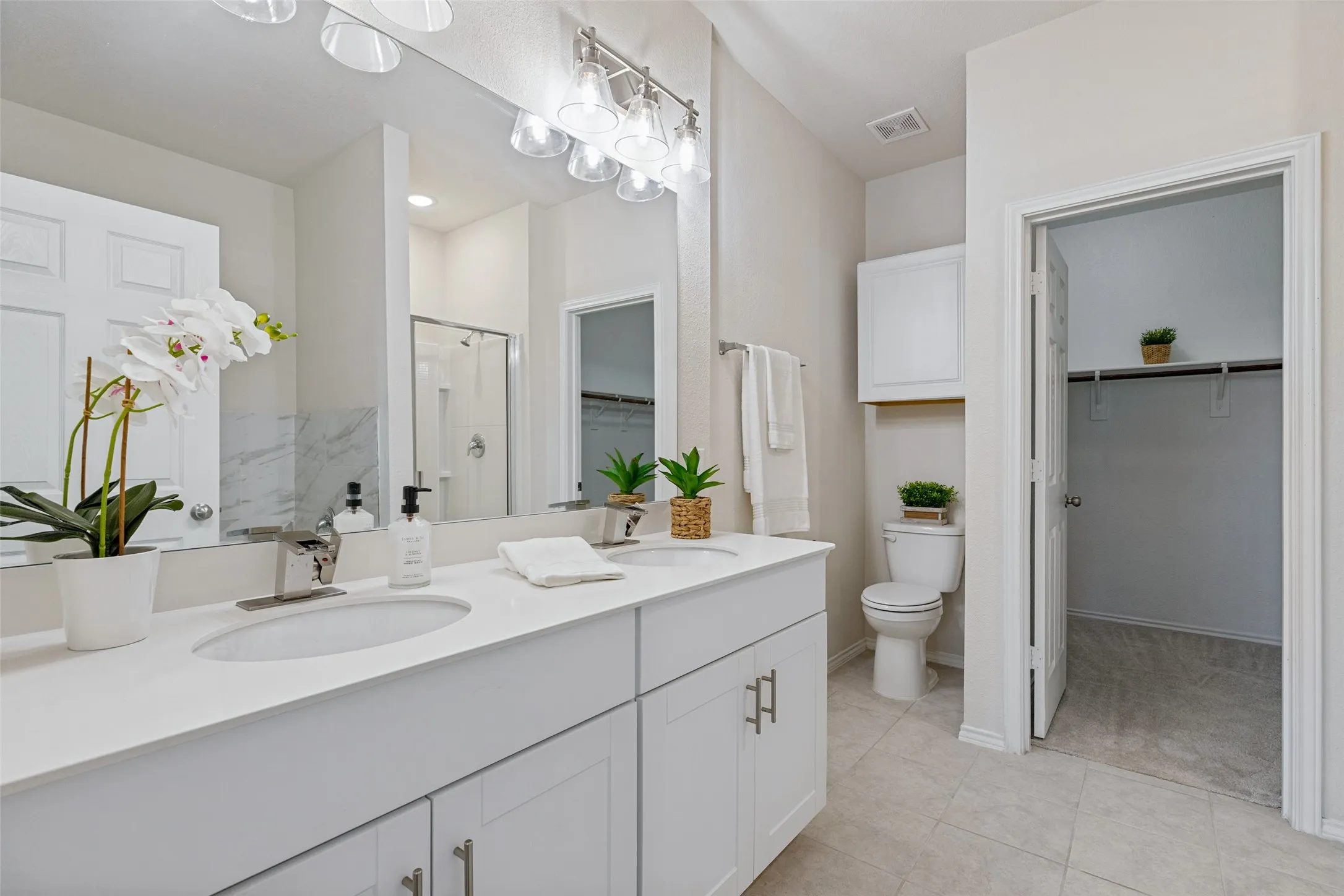 Beautiful master bathroom with dual sinks, quartz countertops, decorative lighting, extra cabinet space, along with a large walk-in closet