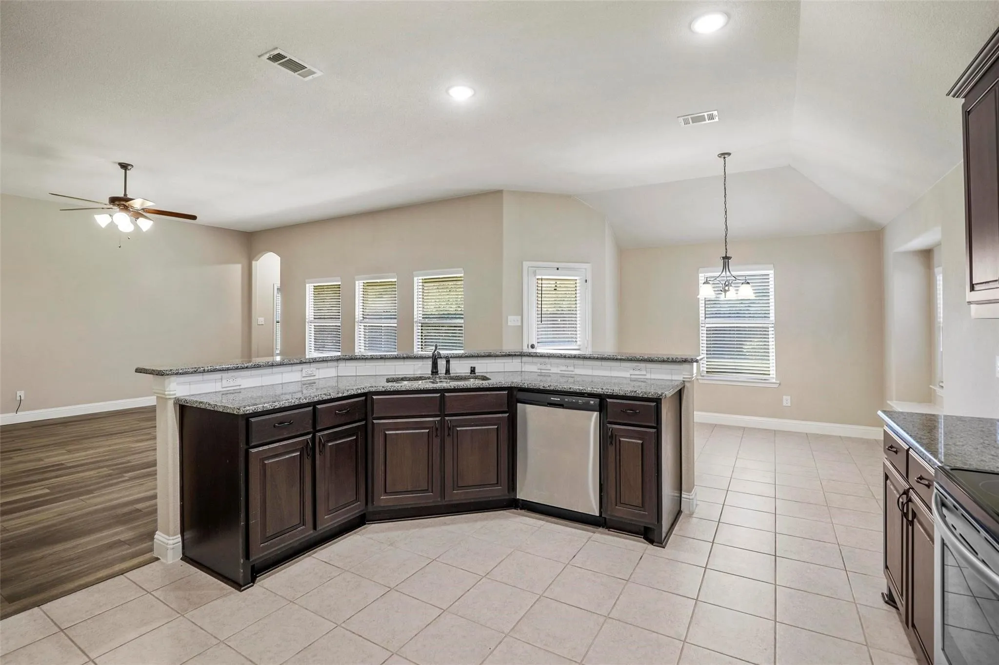 Kitchen featuring dark cabinetry, stone-finish countertops, stainless steel dishwasher, tile flooring, and vaulted ceilings