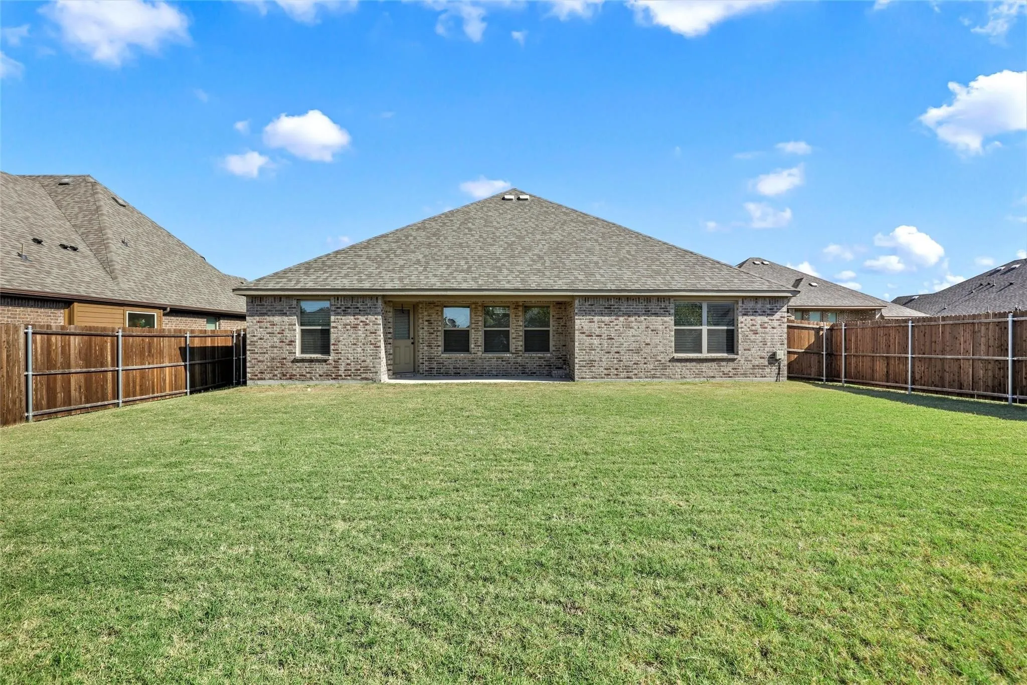 Brick exterior finish, hipped roof, multi-pane windows, and fenced backyard with grass lawn