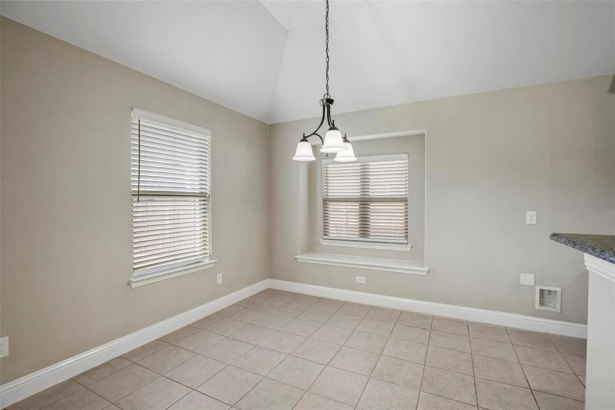 Vaulted ceiling, ceramic tile flooring, built-in window seat, and three-light metal chandelier