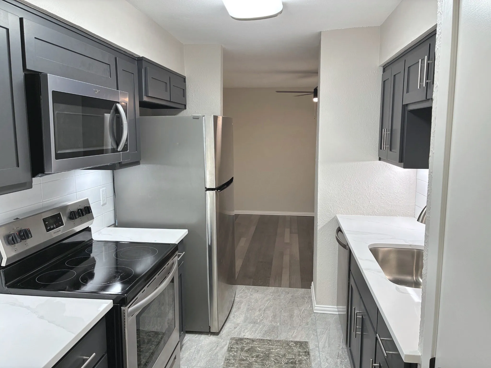 Kitchen featuring dark shaker-style cabinetry, stainless steel appliances, white solid-surface countertops, subway tile backsplash, and stone-finish flooring