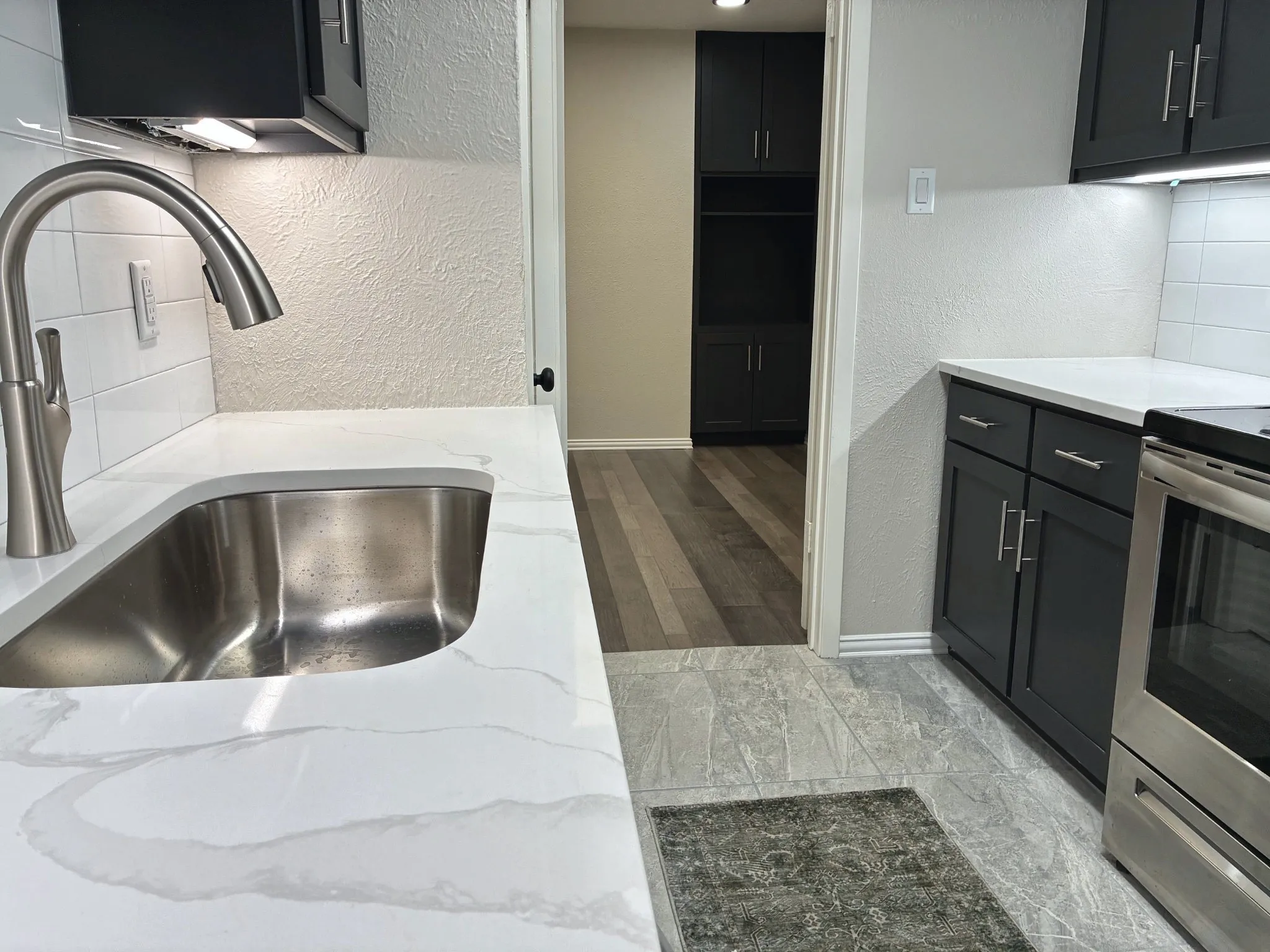 Kitchen featuring quartz countertops, undermount stainless steel sink with pull-down faucet, white subway tile backsplash, dark-toned cabinetry, and stainless steel appliance