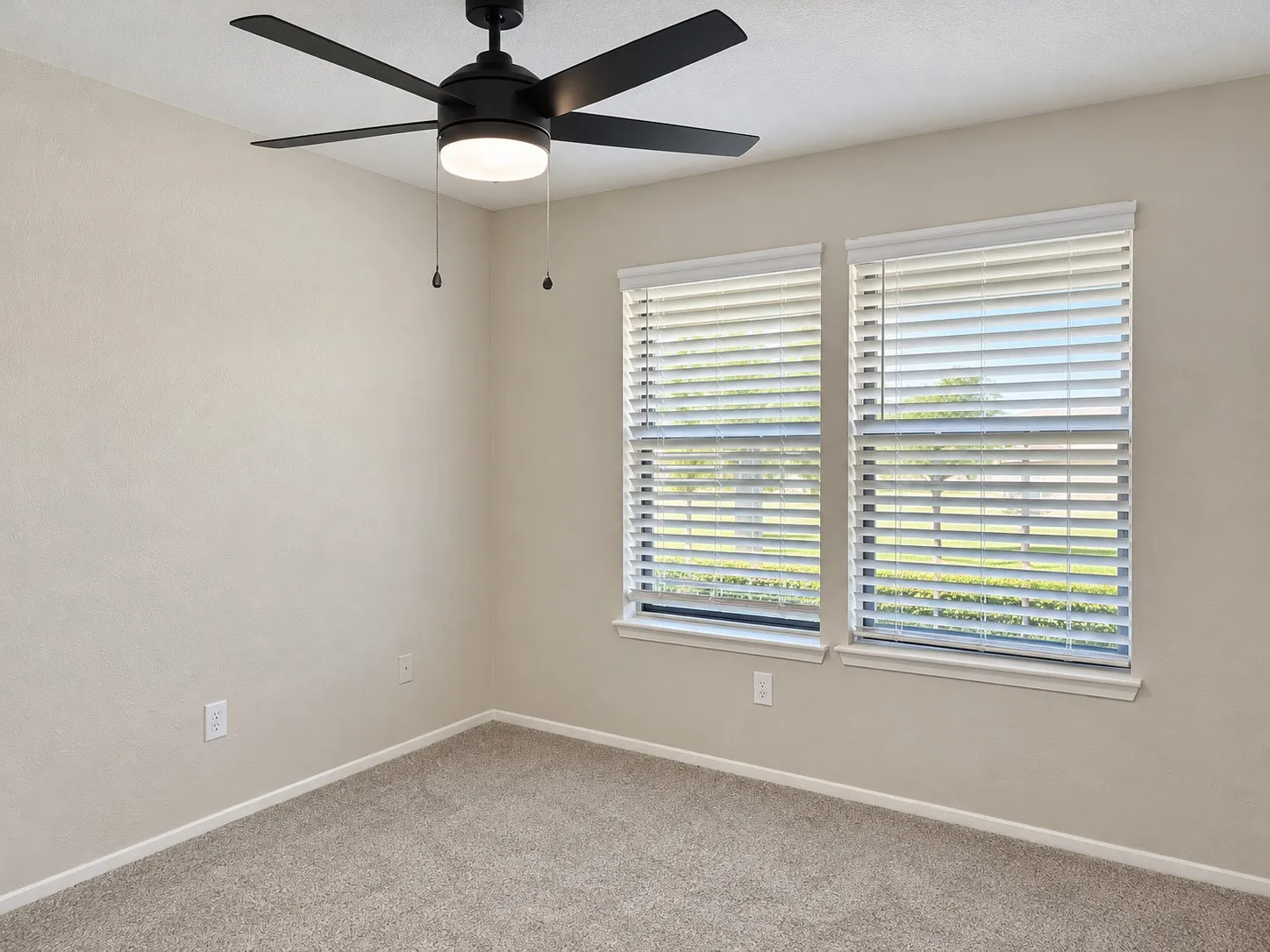 Neutral wall paint, plush carpeting, dual windows with fitted blinds, and a contemporary matte black ceiling fan with integrated lighting