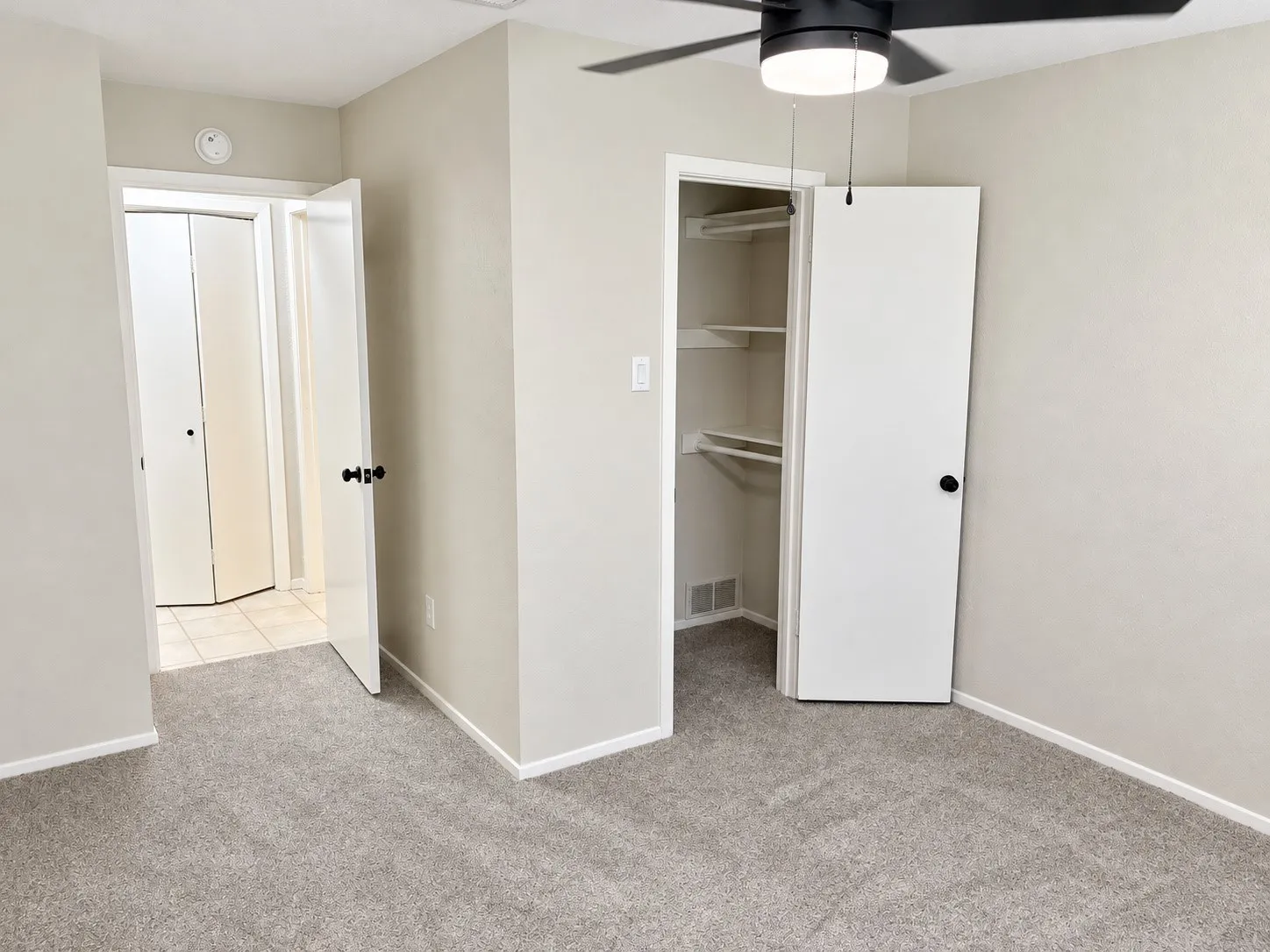 Neutral-toned carpeting, matte black hardware, built-in closet shelving, and a ceiling fan with integrated light fixture