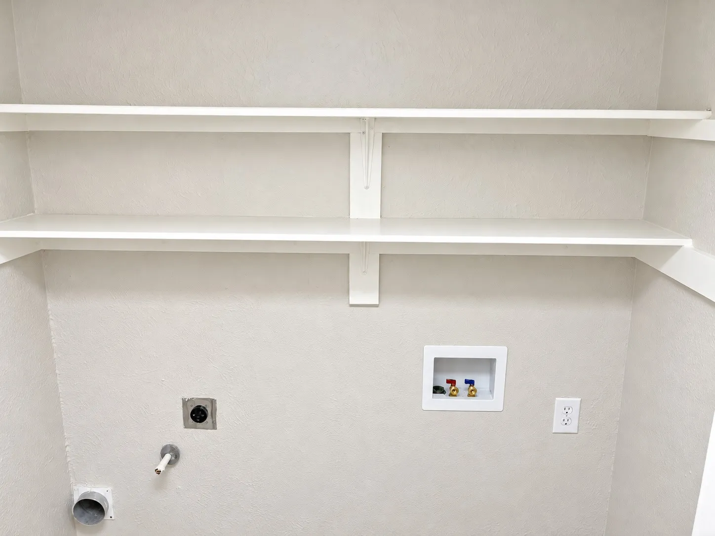 Utility area featuring two levels of built-in shelving, recessed water supply valves, and dedicated electrical and venting connections