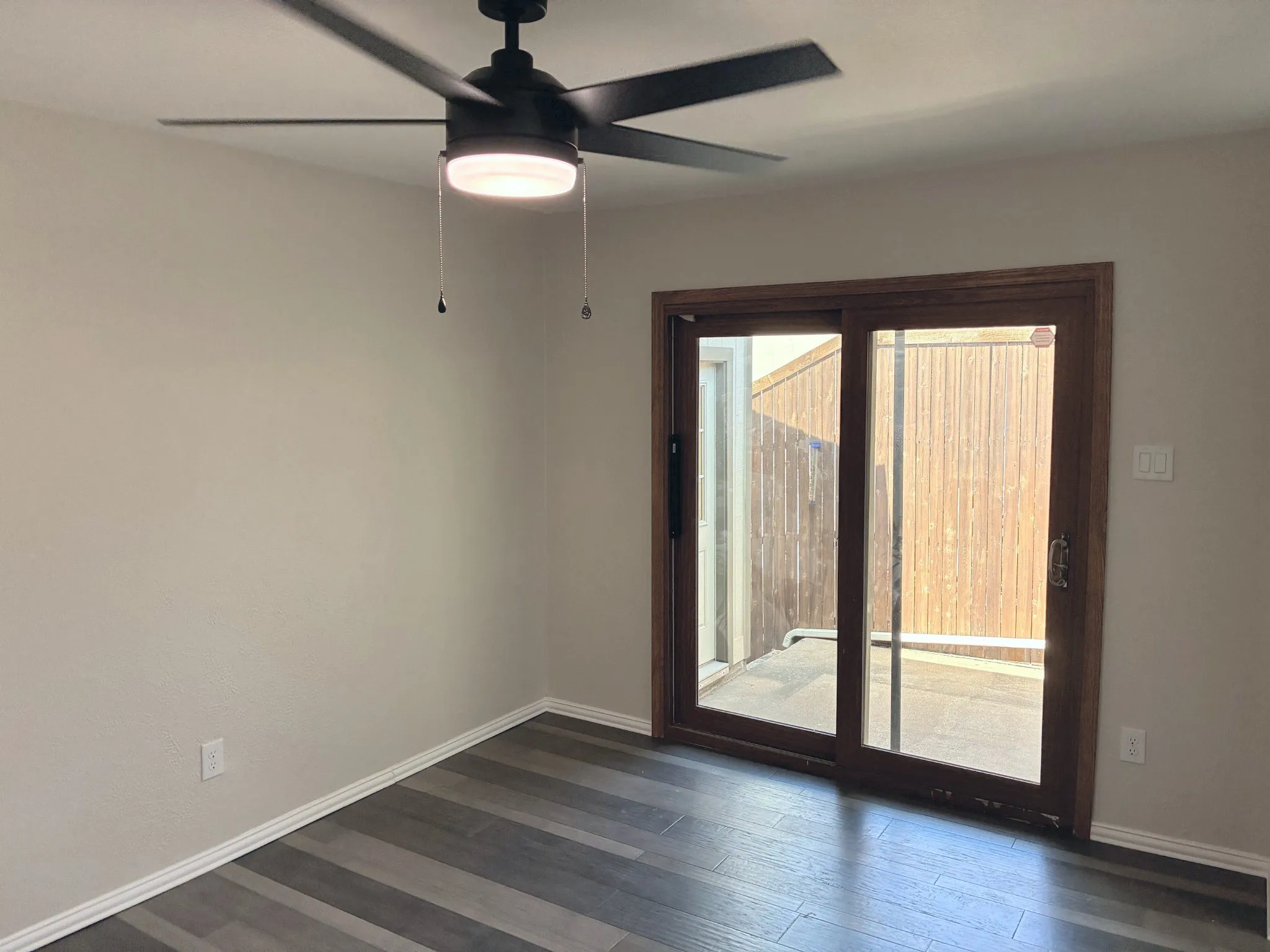 Multi-tone wood-finish flooring, matte black ceiling fan with integrated lighting, and glass-paneled sliding door with wooden frame
