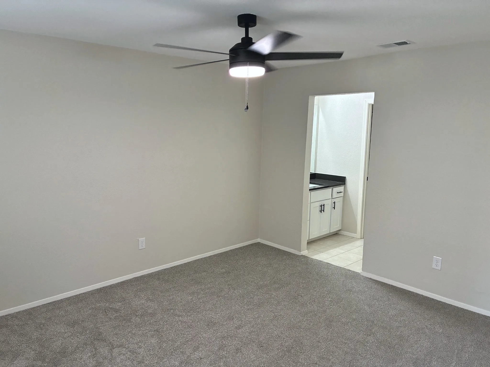 Neutral-toned carpeting, matte black ceiling fan with integrated LED lighting, and vanity featuring a solid surface countertop with dark hardware