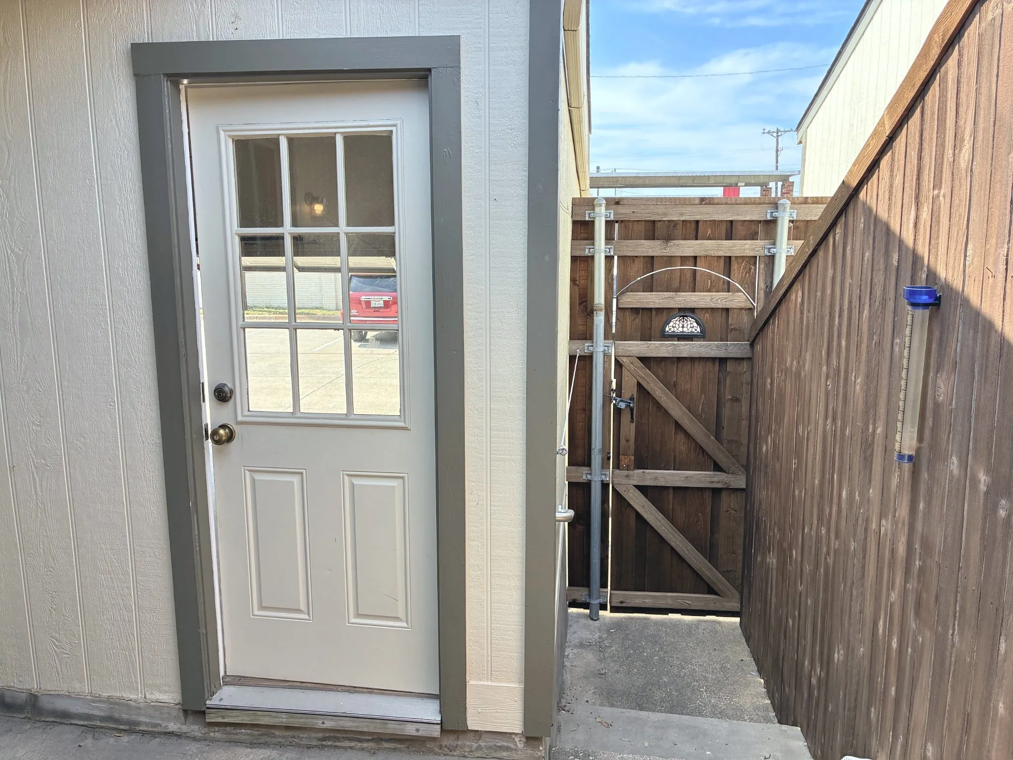 Exterior access door with nine-lite window pane, set within vertical-paneled siding, complemented by a wood-plank privacy gate and concrete walkway