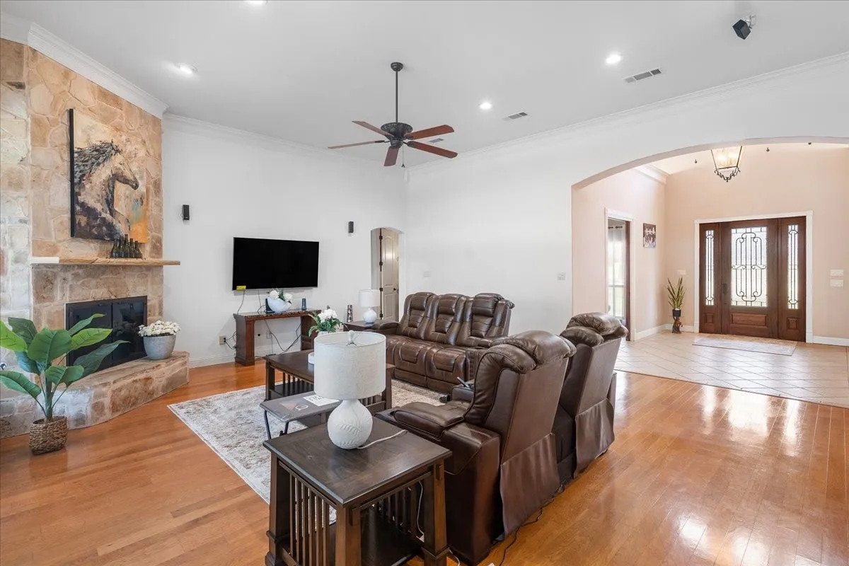 Living room featuring wood-finish flooring, a floor-to-ceiling stone-surround fireplace with a wooden mantel, recessed lighting, and an arched entryway leading to a foyer with a wood-framed glass-paneled door