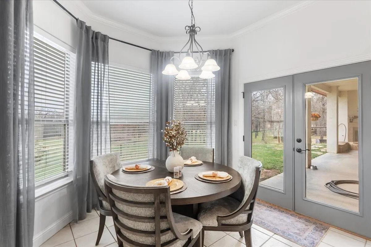 Bay window with multi-pane windows, crown molding, tiered metal chandelier, and full-lite glass double doors leading to a covered patio