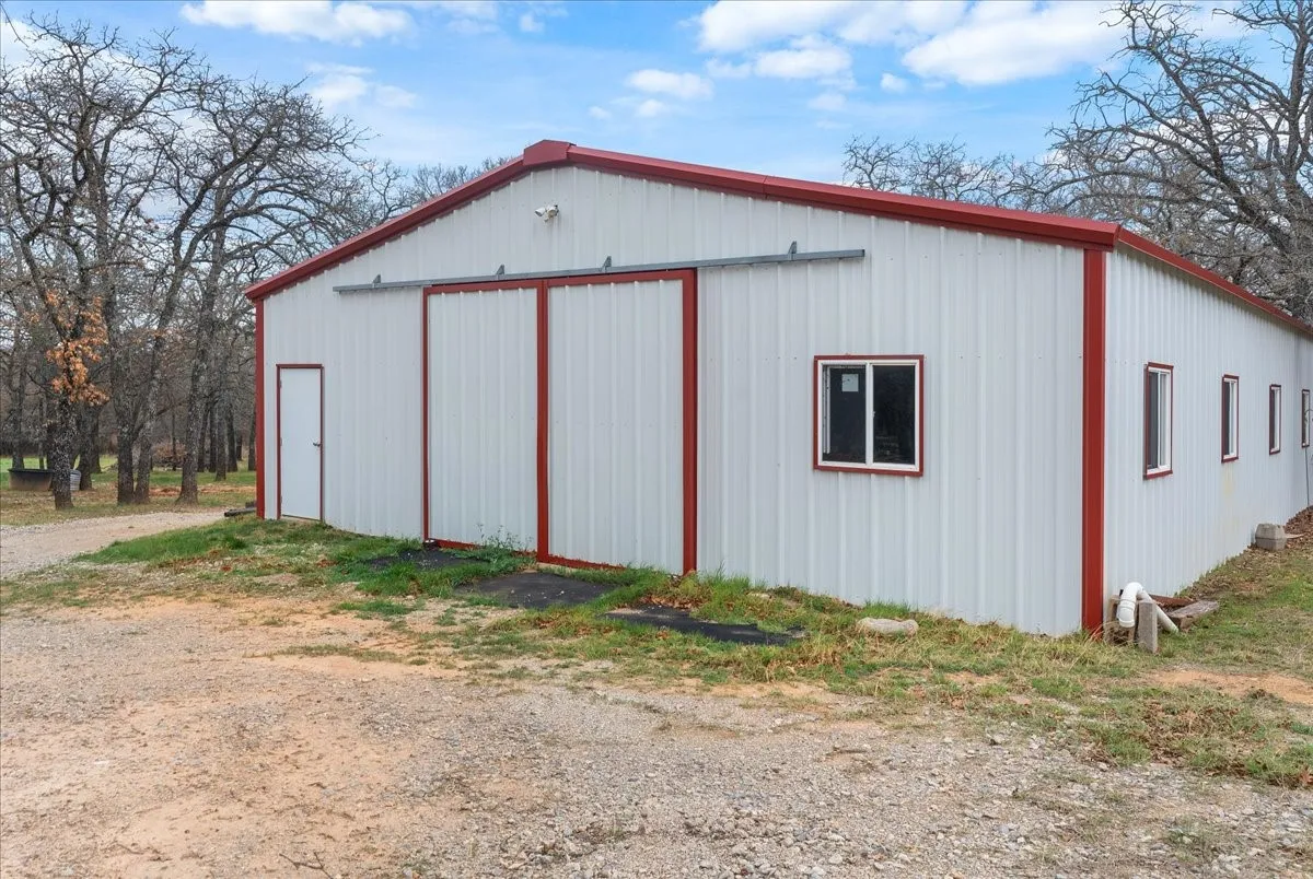 Modern metal-frame agricultural or commercial building featuring a distinctive peaked roof with red trim accents, white corrugated metal siding, and multiple window openings for natural light