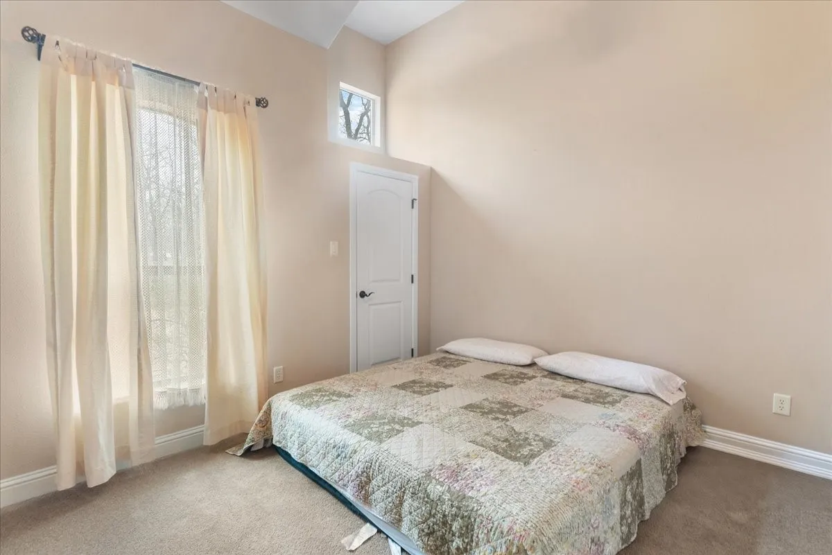 Guest House. Bright secondary bedroom featuring neutral wall finishes, carpeted flooring, and abundant natural light from a sliding glass door with sheer curtains