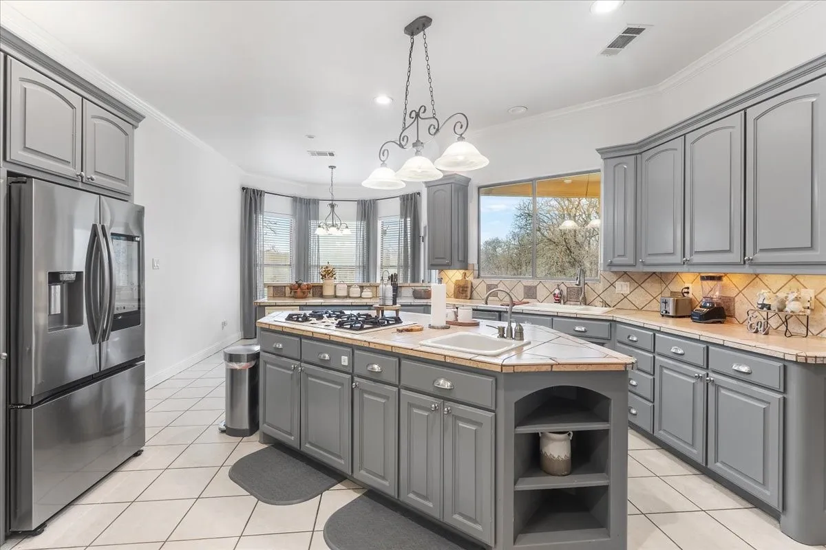 Kitchen featuring grey cabinetry, a central island with a built-in cooktop, tile countertops, recessed lighting, and stainless steel appliances