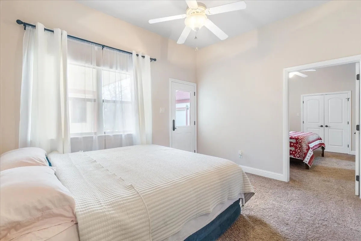 Vaulted ceiling with integrated ceiling fan, carpeted flooring, and exterior glass-panel door