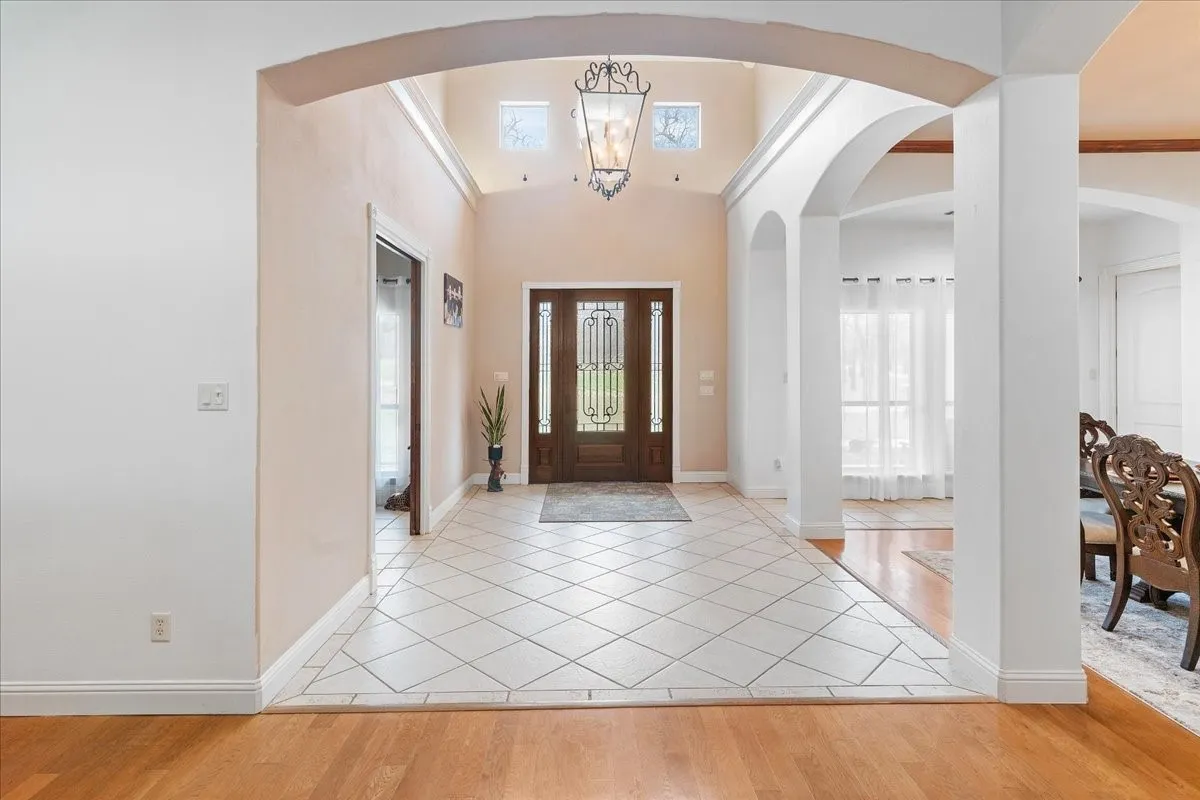 Grand entryway featuring high ceilings, a decorative wrought-iron chandelier, porcelain tile flooring set on a diagonal, and a wooden front door with glass insets framed by architectural arches