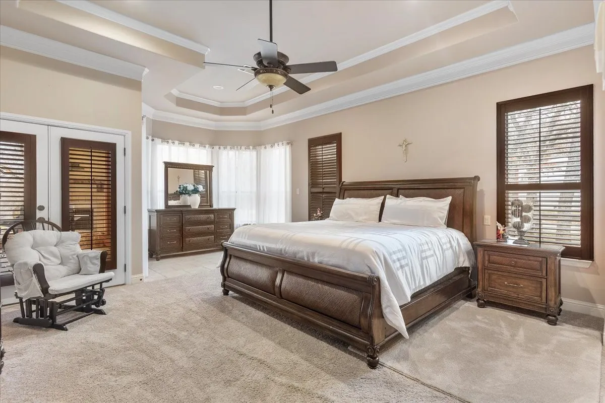 Tray ceiling with crown molding, ceiling fan, carpeted flooring, and dark wood-finish plantation shutters