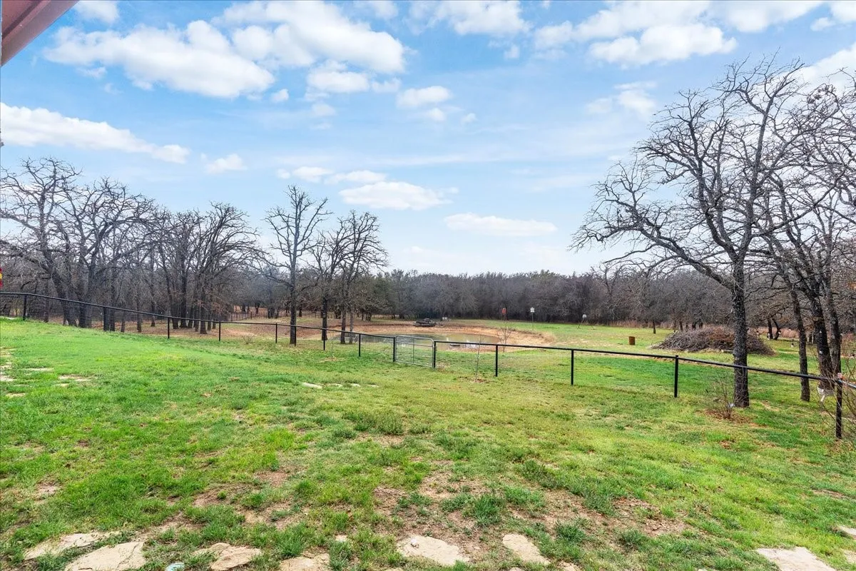 Expansive green space featuring mature trees, a perimeter fence, and a natural pond