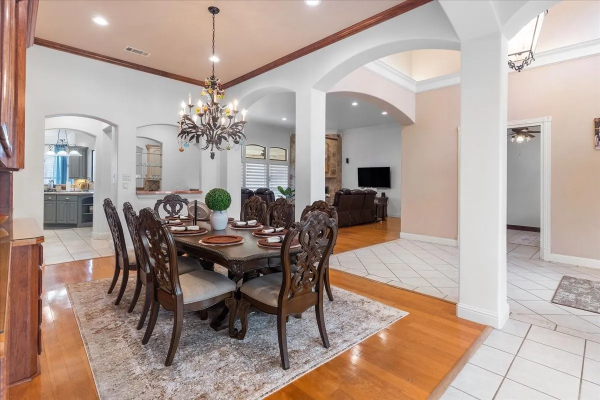 Dining area featuring wood-finish flooring, decorative ceiling molding, arched architectural openings, and a multi-tiered metal chandelier