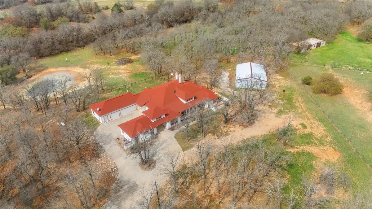 Aerial view of property featuring a multi-gabled roofline, concrete driveway, attached garage, detached metal building, and private pond