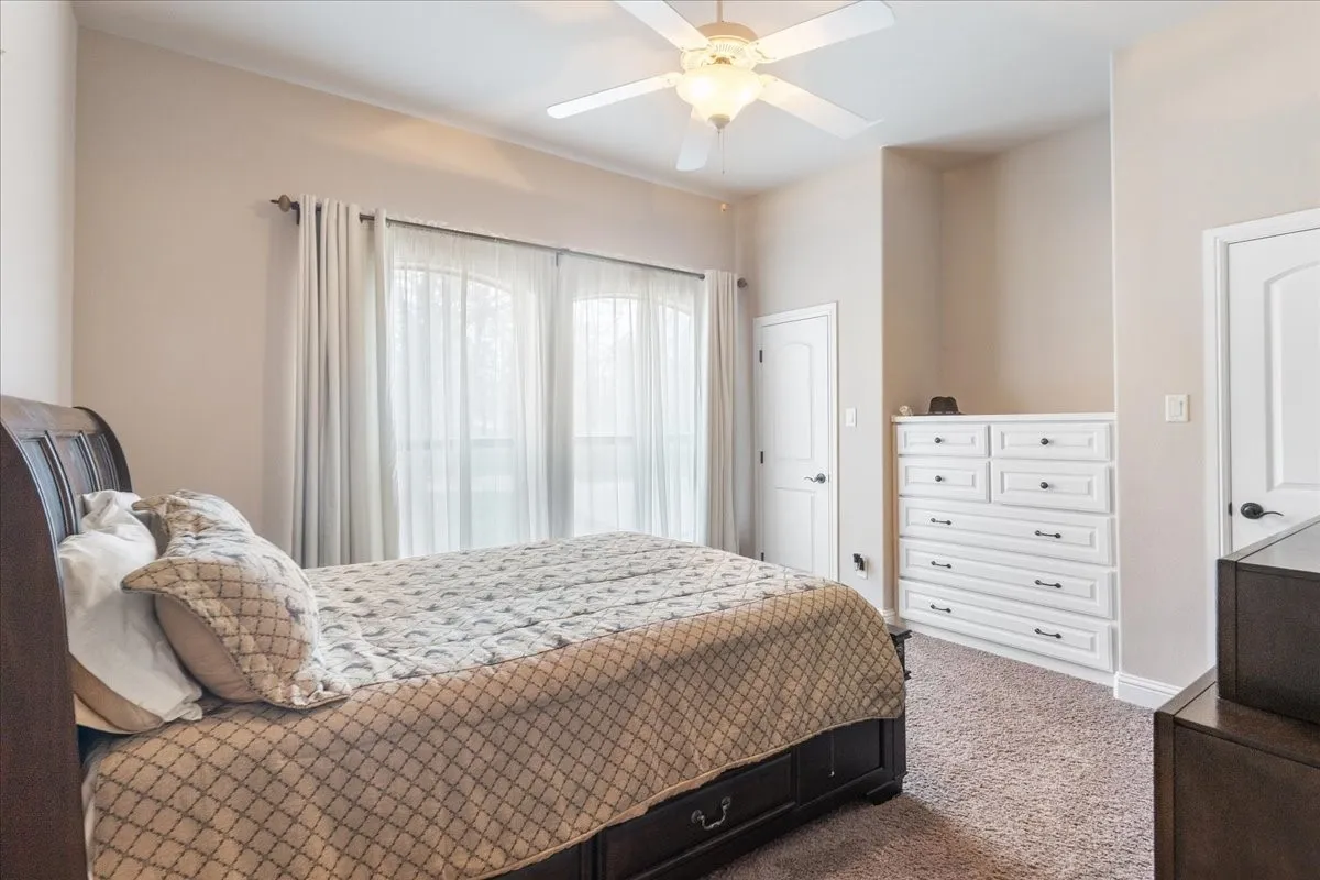Carpeted room featuring a ceiling fan with integrated lighting, built-in dresser with multiple drawers, and arched patio doors
