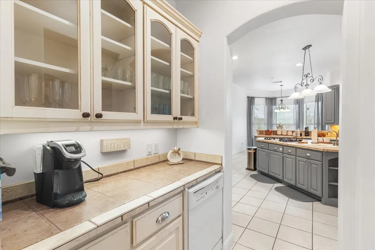 Custom off-white cabinetry with glass-front uppers, ceramic tile countertops, built-in dishwasher, and arched architectural detailing