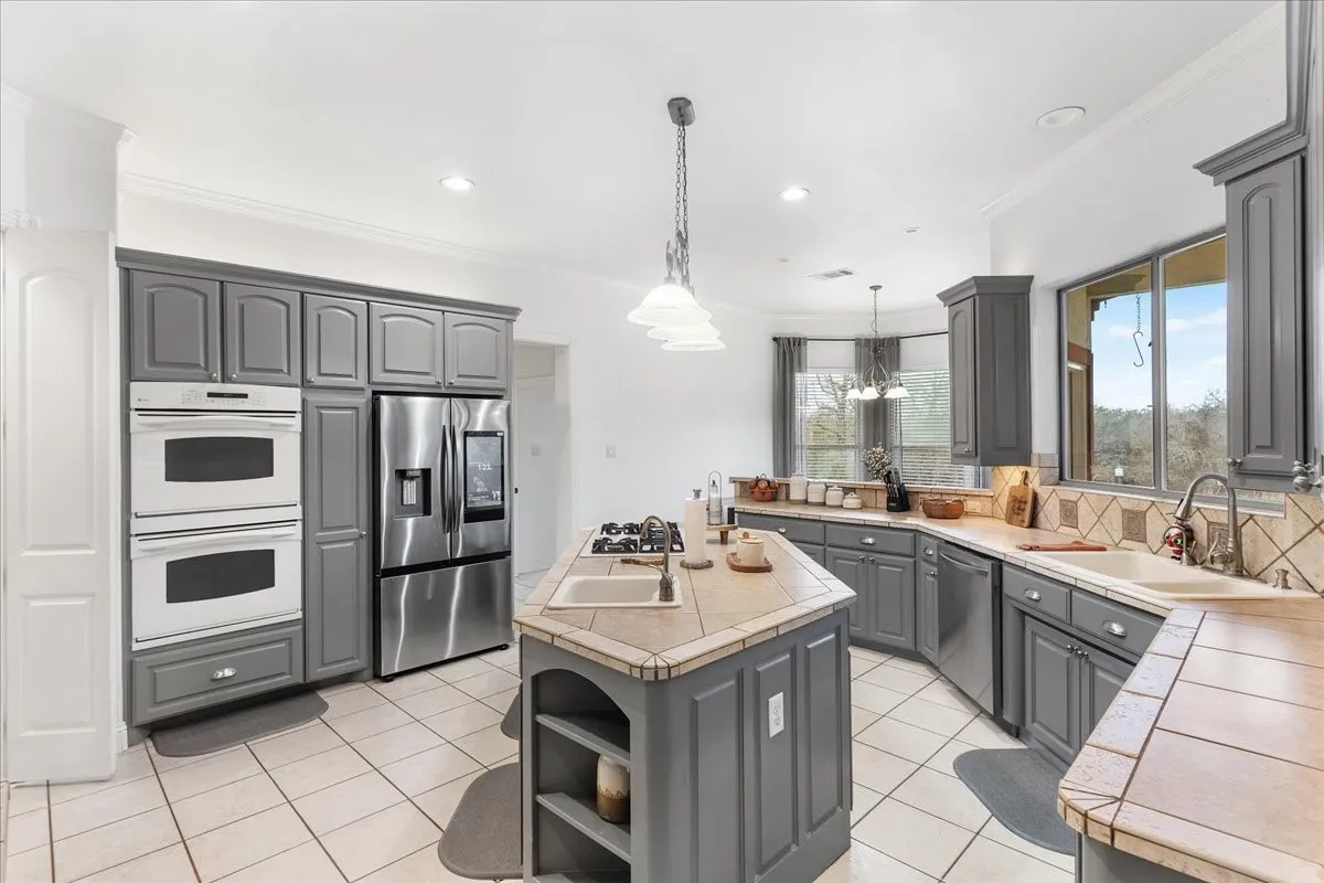 Kitchen featuring gray cabinetry, tile flooring, built-in double ovens, stainless steel refrigerator, and an island with a gas cooktop