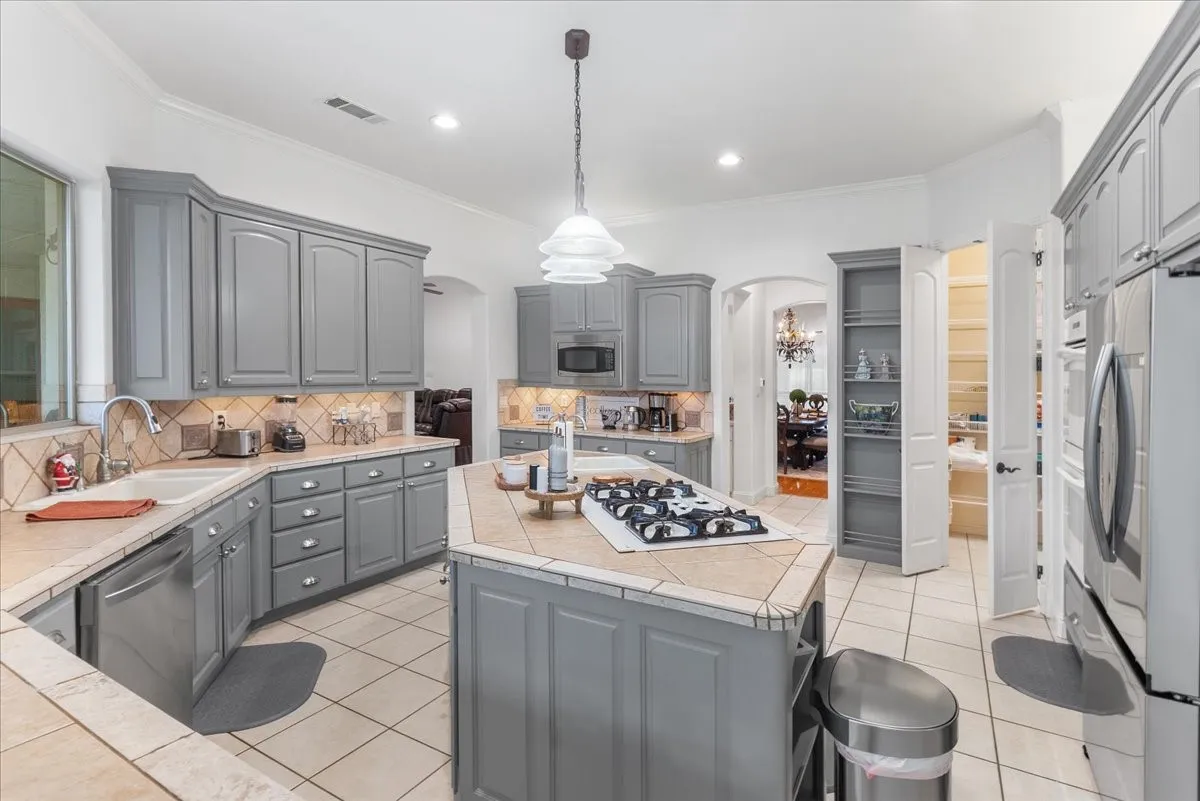 Kitchen featuring grey shaker-style cabinetry, center island with a built-in cooktop, tiled countertops, stainless steel appliances, and tile flooring