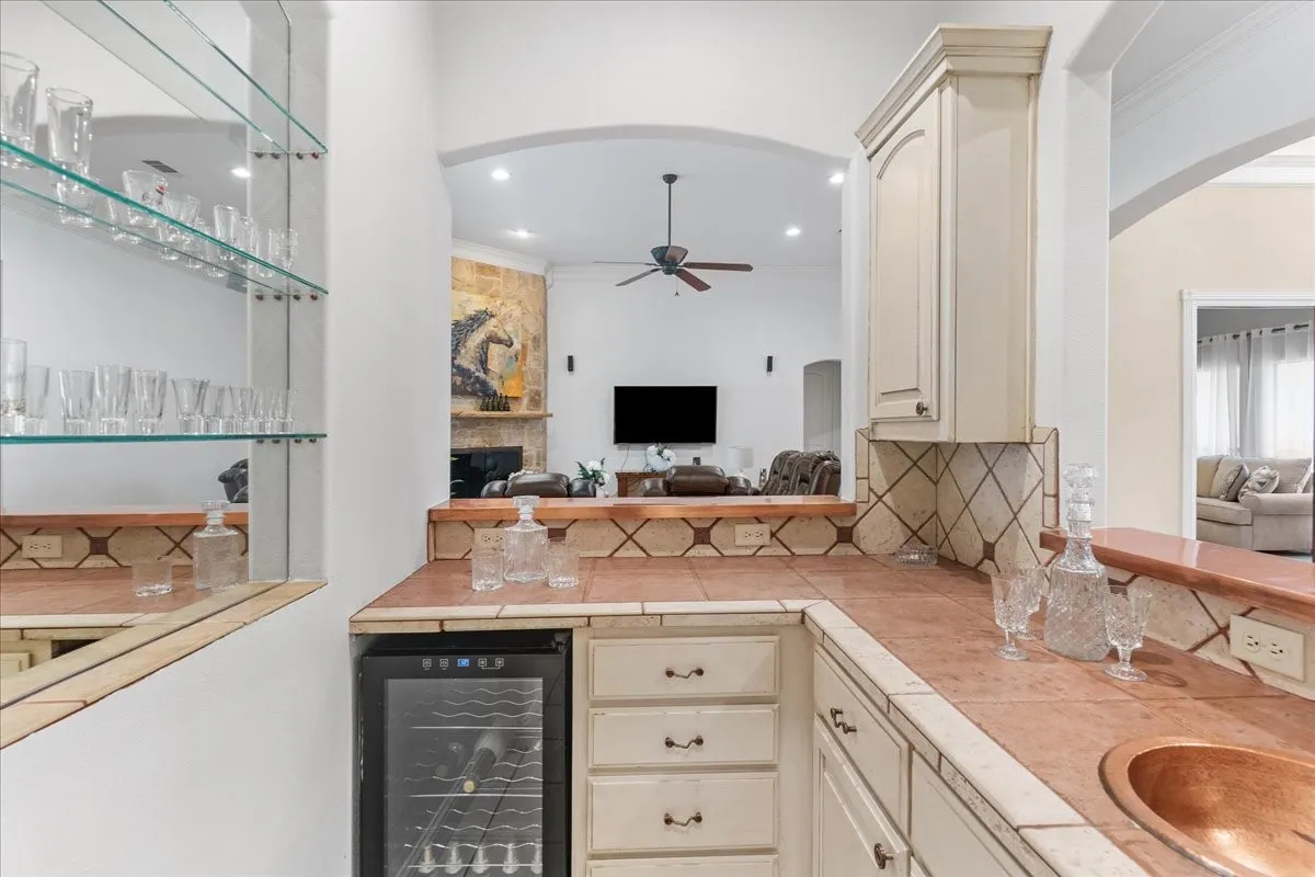 Built-in wet bar featuring tile countertops, copper sink, glass shelving, cabinetry, and a dedicated beverage cooler