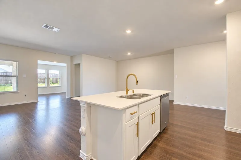 Central island featuring a dual-basin sink with a gold-finish faucet, white cabinetry, and a light-toned countertop