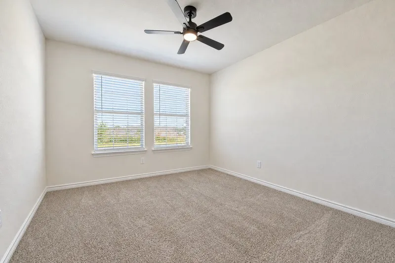 Spacious room featuring neutral carpet flooring, two windows with blinds, a ceiling fan with integrated lighting, and light-toned walls