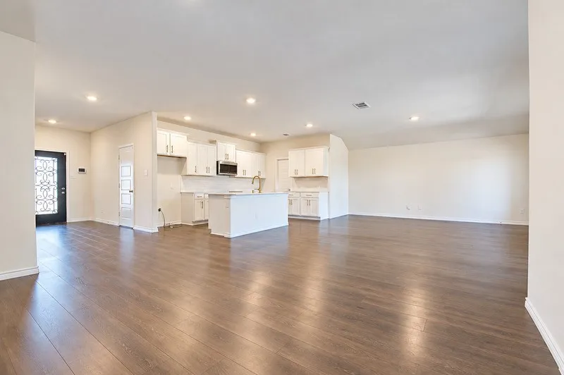 Spacious open-concept living area with wood-finish flooring, recessed lighting, and a kitchen featuring white cabinetry, a central island, and a subway tile backsplash