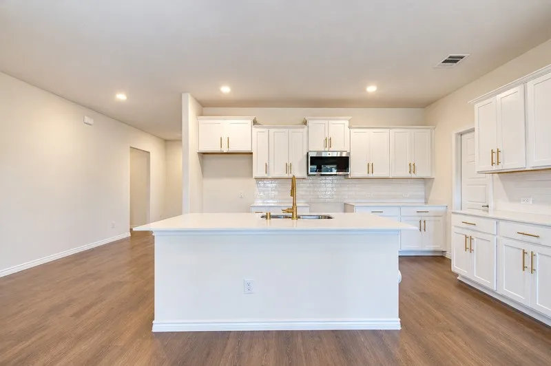 Modern kitchen featuring white cabinetry, a large center island with a sink, stainless steel microwave, and wood-finish flooring