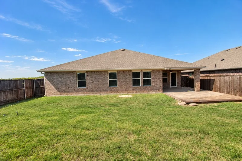 Expansive backyard with a manicured lawn, full brick exterior, covered patio, and wood privacy fencing