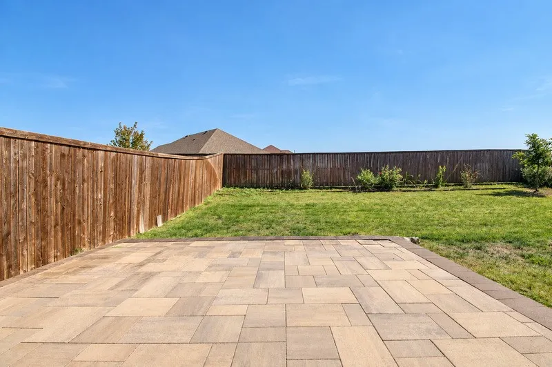 Expansive paver patio with a contrasting border, leading to a lawn area with a wood privacy fence