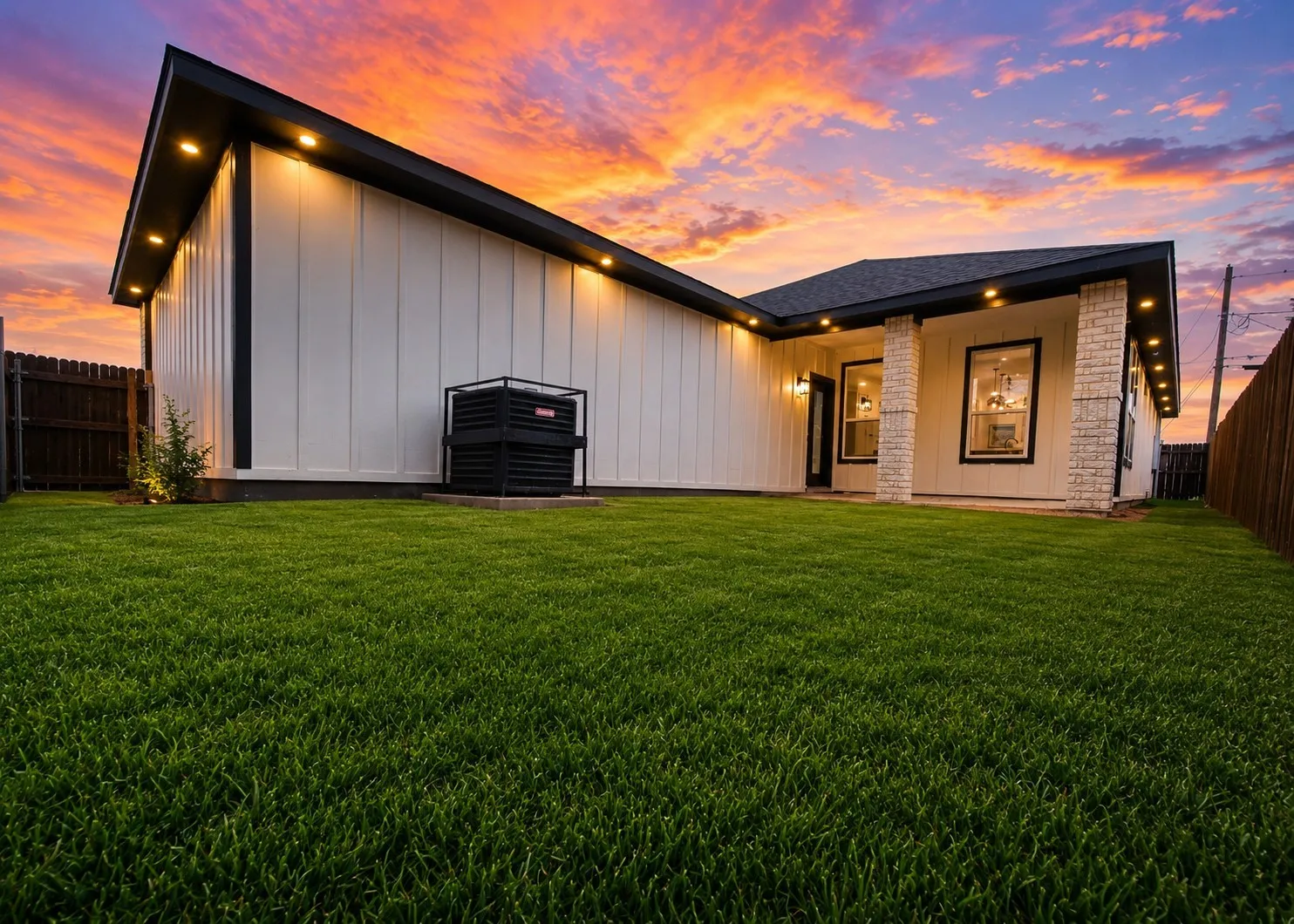 Board-and-batten exterior siding, masonry column accents, recessed soffit lighting, and manicured lawn