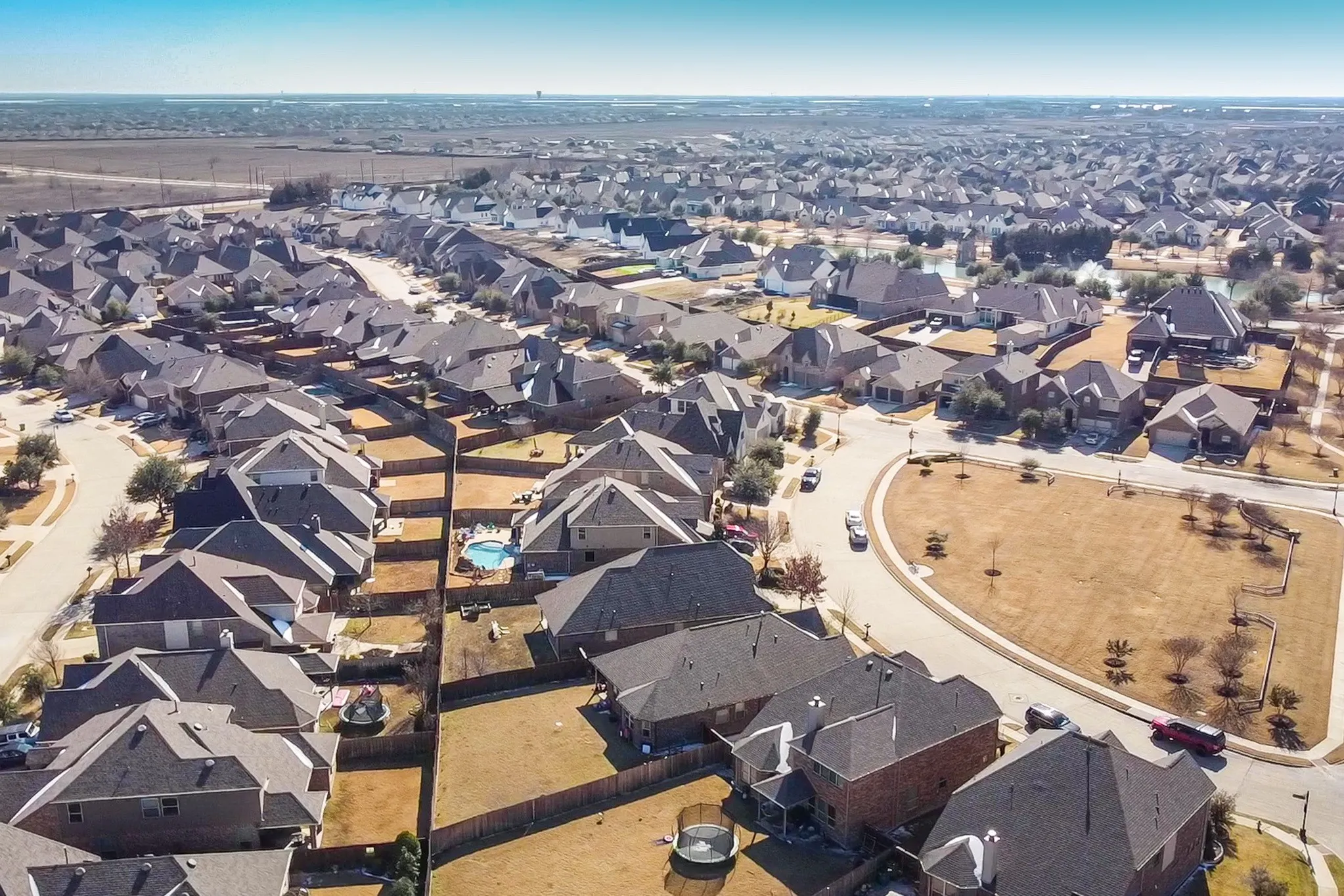 Aerial view of a residential neighborhood featuring multiple single-family dwellings, asphalt streets, and fenced backyards