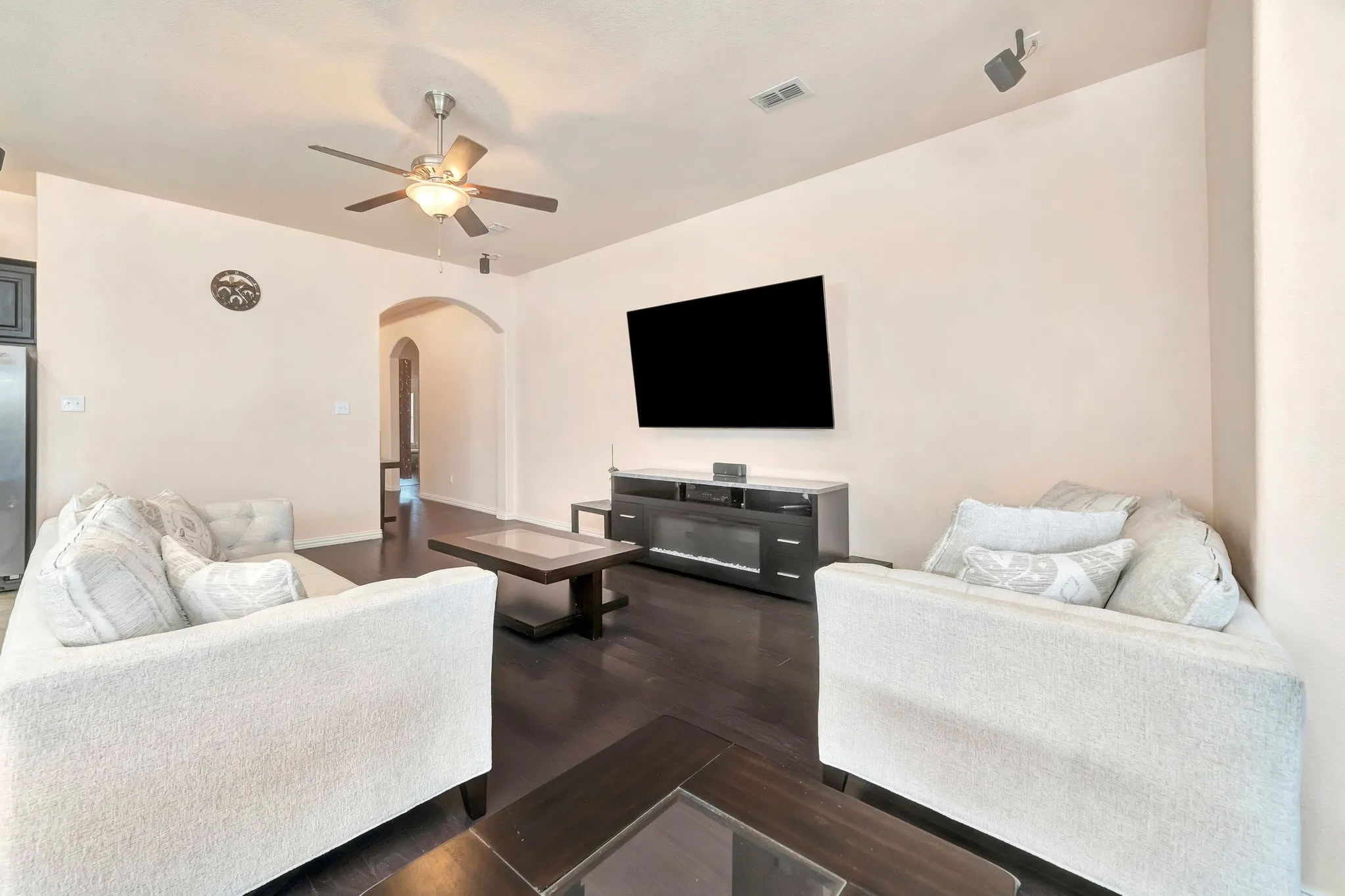 Living area featuring wood-finish flooring, a ceiling fan with integrated light, and an arched doorway