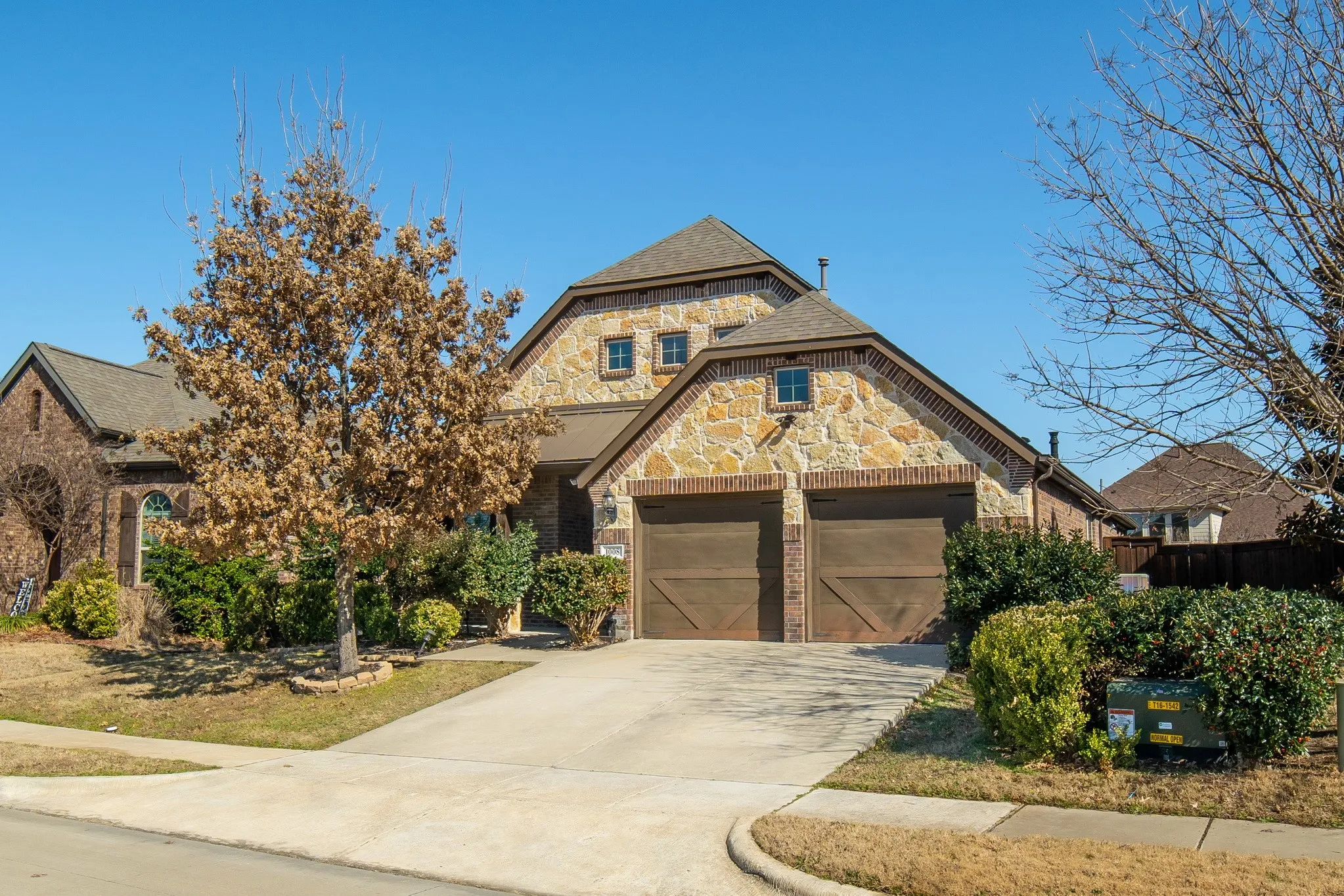 Exterior featuring stone masonry facade, dual carriage-style garage doors, multi-gabled roofline, and concrete driveway