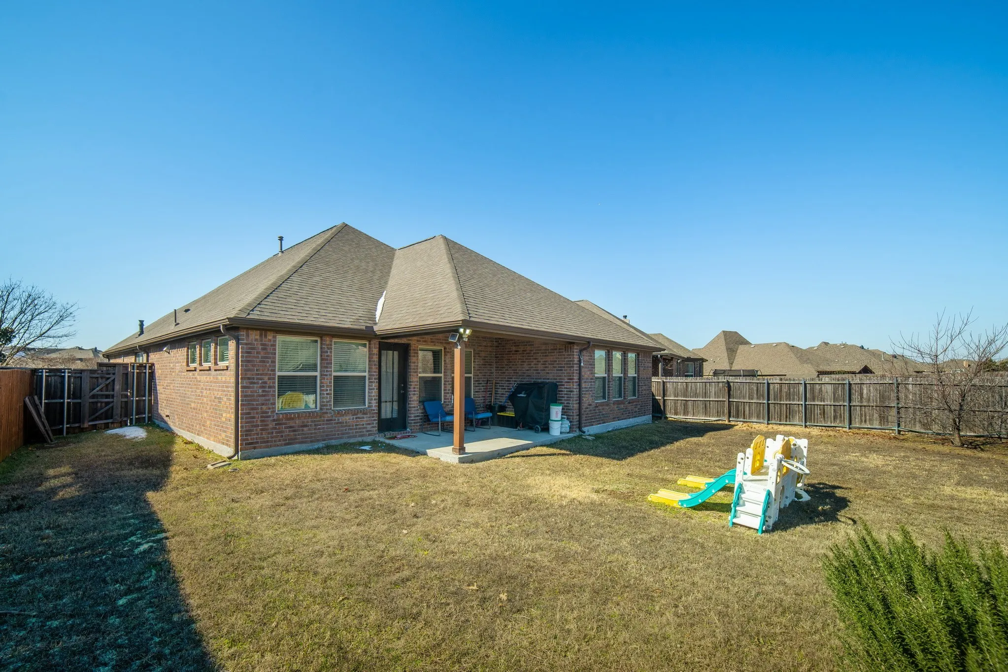 Brick exterior featuring a covered rear patio, hip roofline, and wood privacy fencing